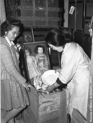 Japanese American women packing dolls and dishes in storage crate, PI-28064
